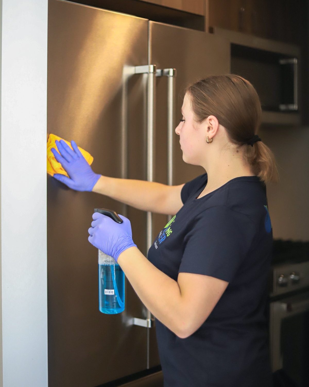 Cleaning Master professional wiping down a stainless steel refrigerator in an empty apartment