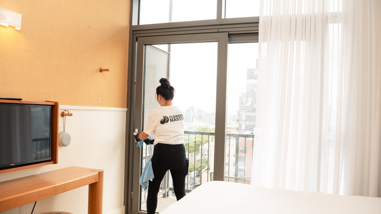 Cleaning Master professional cleaning a glass balcony door with the city beyond