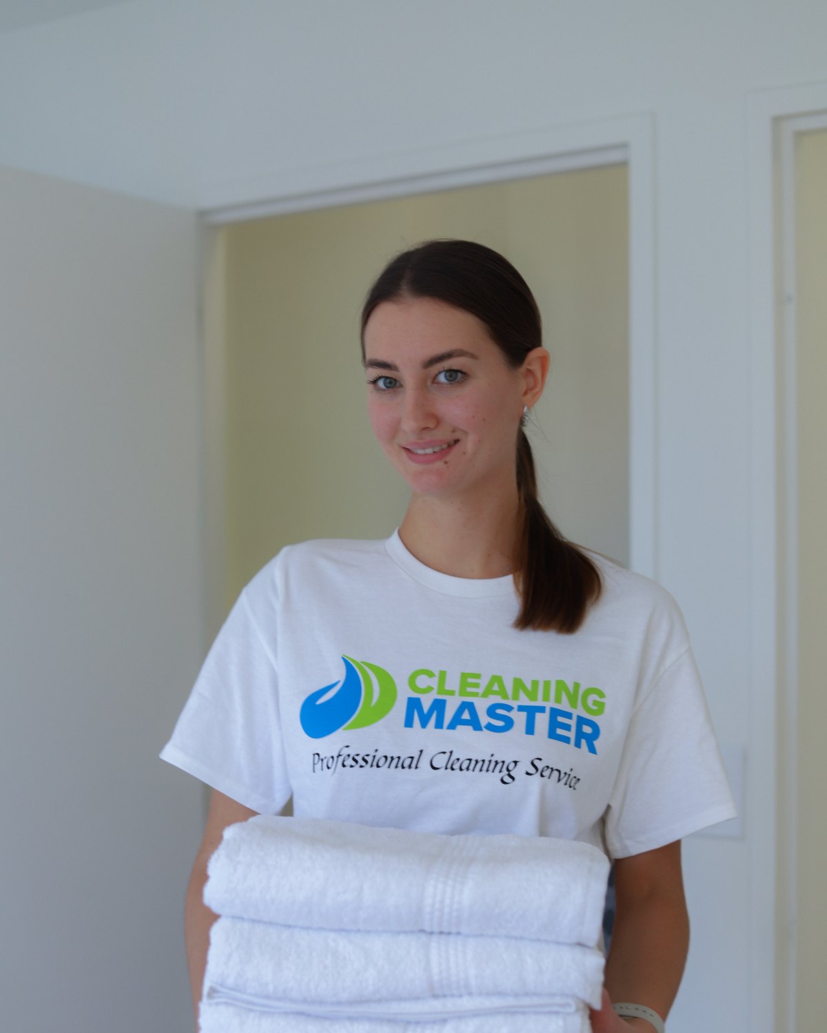 Smiling Cleaning Master professional holding a stack of fresh white towels