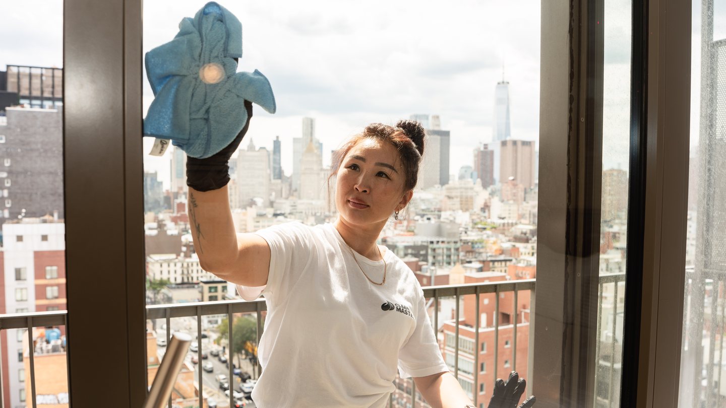 Cleaning Master professional wiping a large window with a microfiber cloth, skyline behind