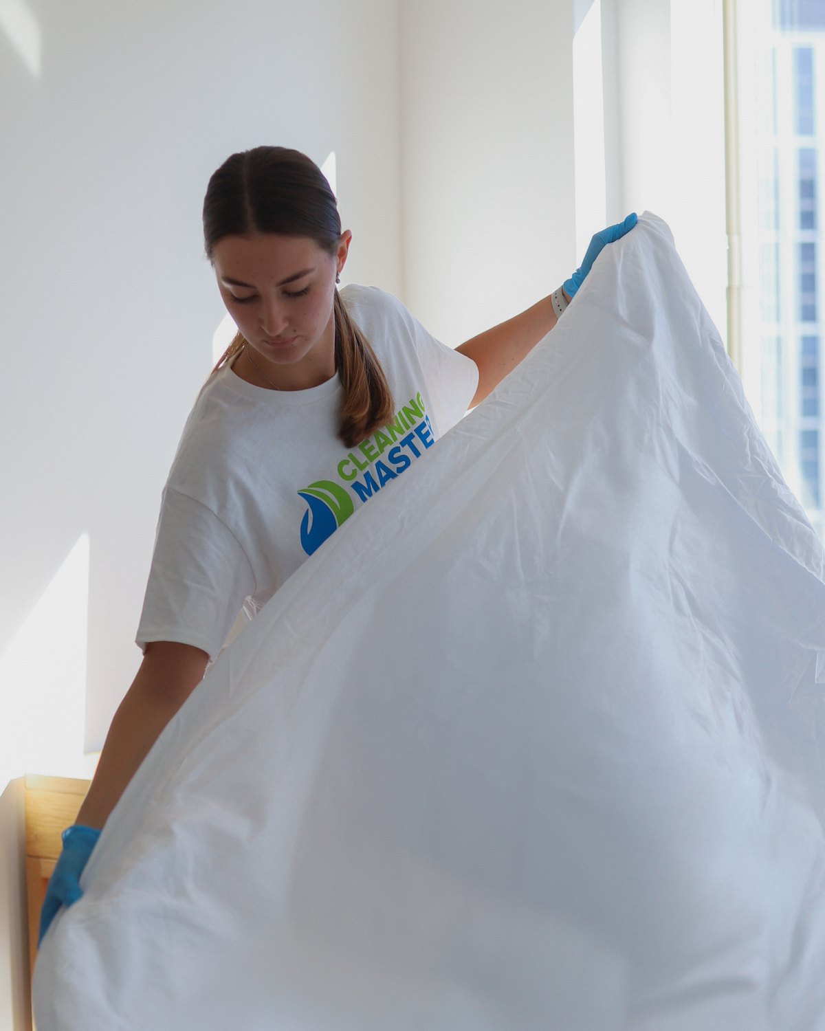 Cleaning Master professional changing a fresh white sheet in a hotel-style guest room