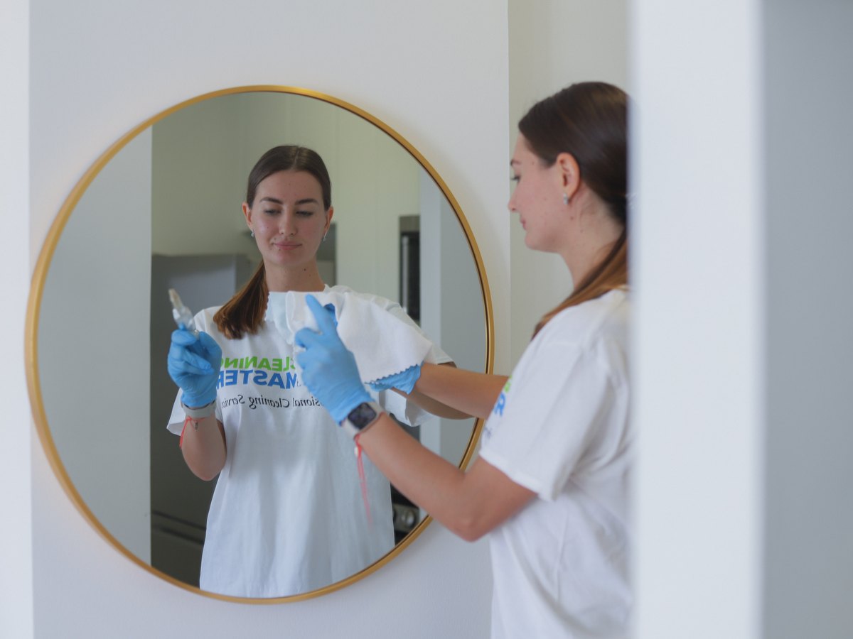 Cleaning Master professional polishing a round wall mirror with a microfiber cloth