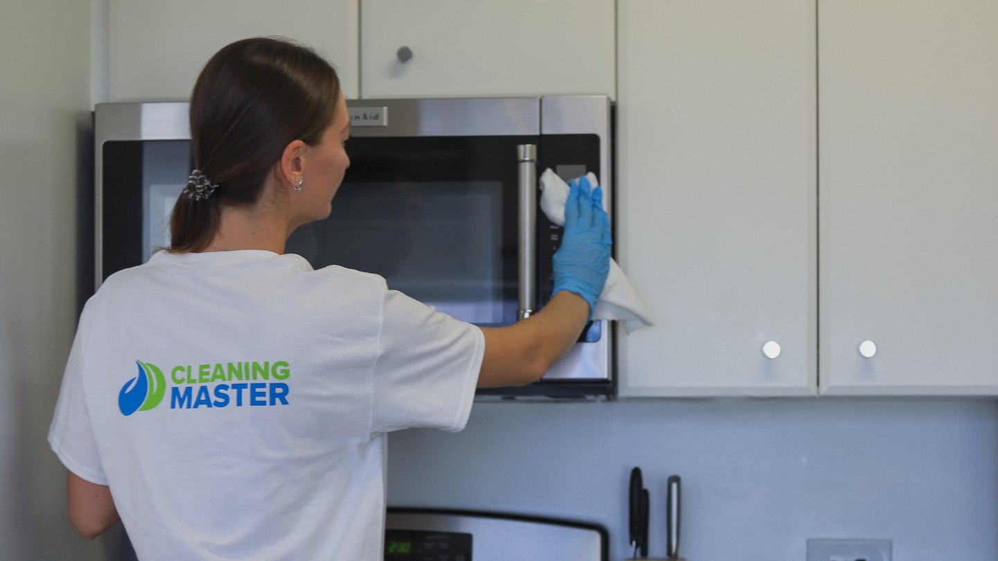 Cleaning Master professional wiping a stainless steel microwave in a commercial kitchen